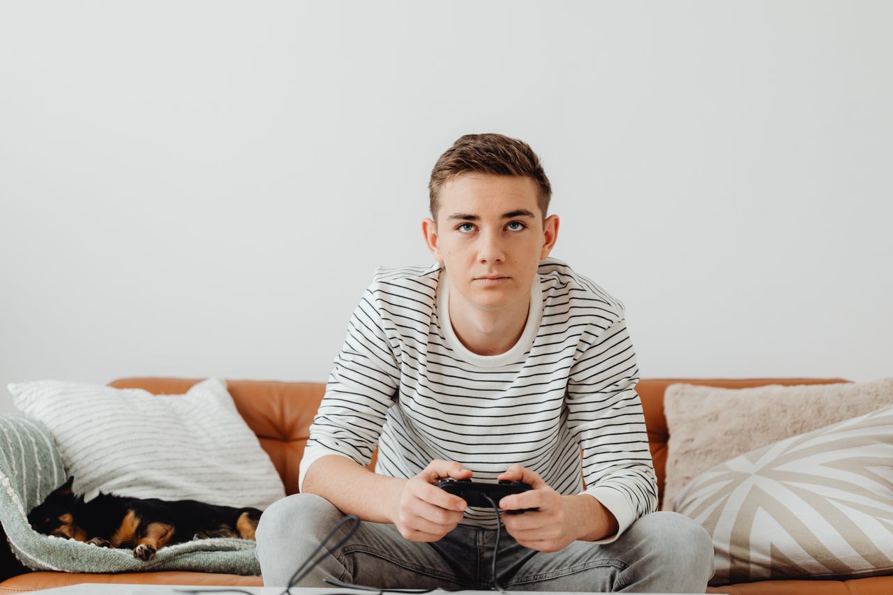 ソファでゲームのコントローラーを持つ男の子／中高生のゲームのイメージ