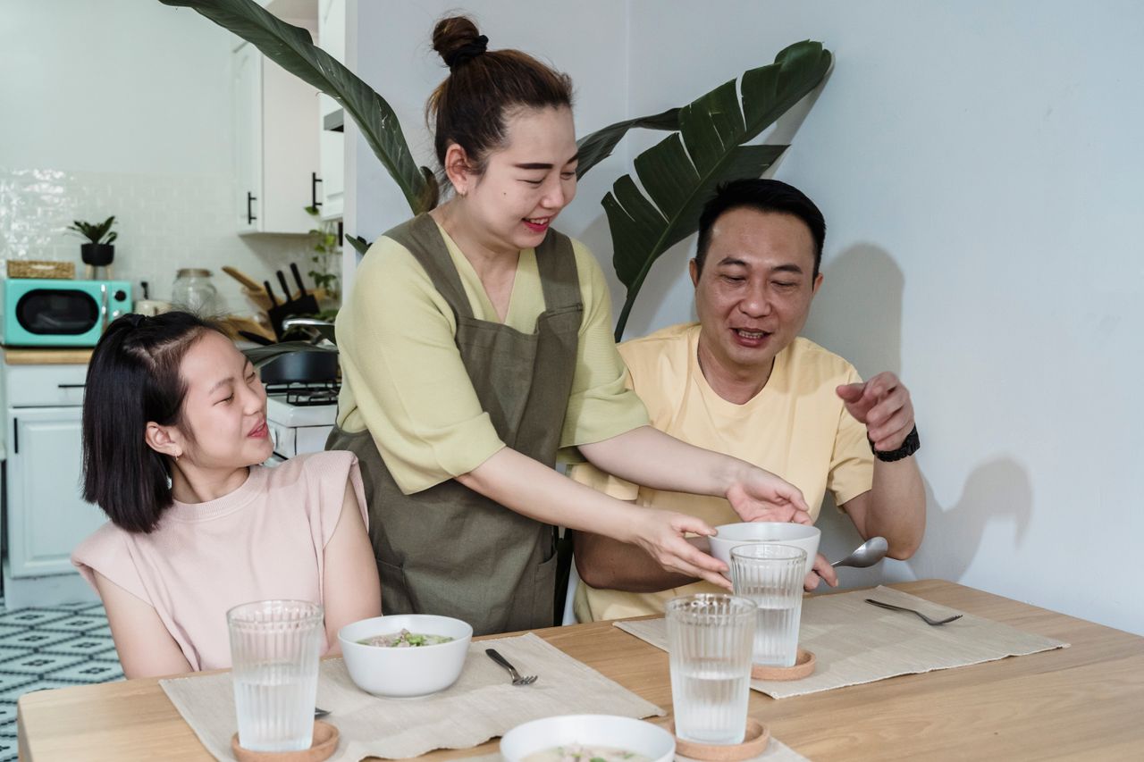 家族の食卓を囲む母と娘と父／帰省した子と囲むいつものごはんのイメージ